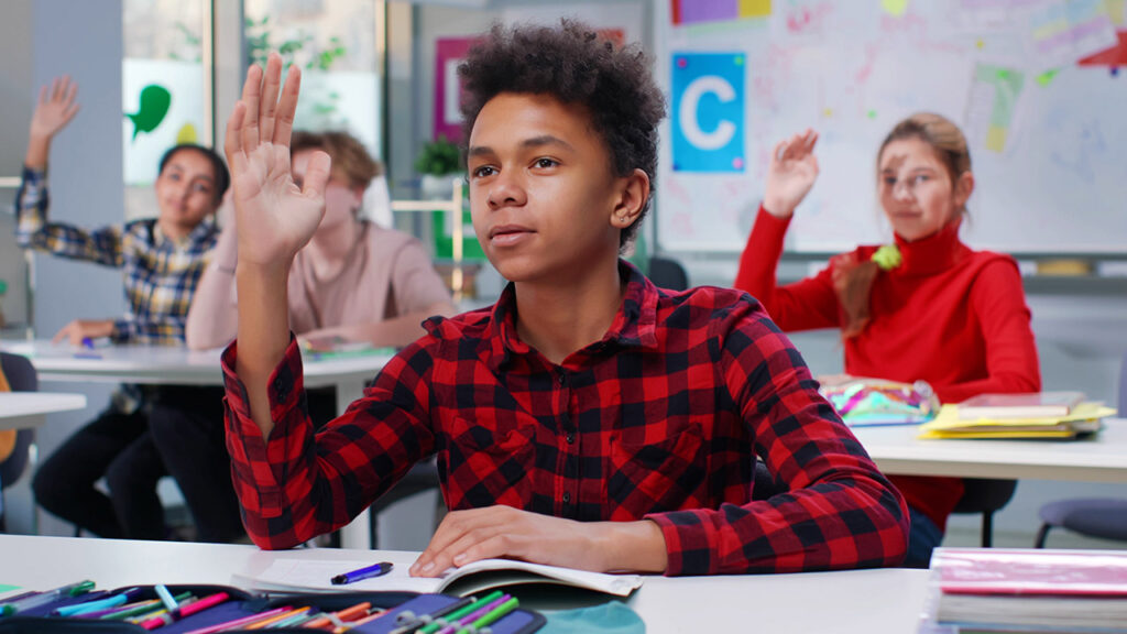 Multiethnic teen students raise hands to answer teacher question