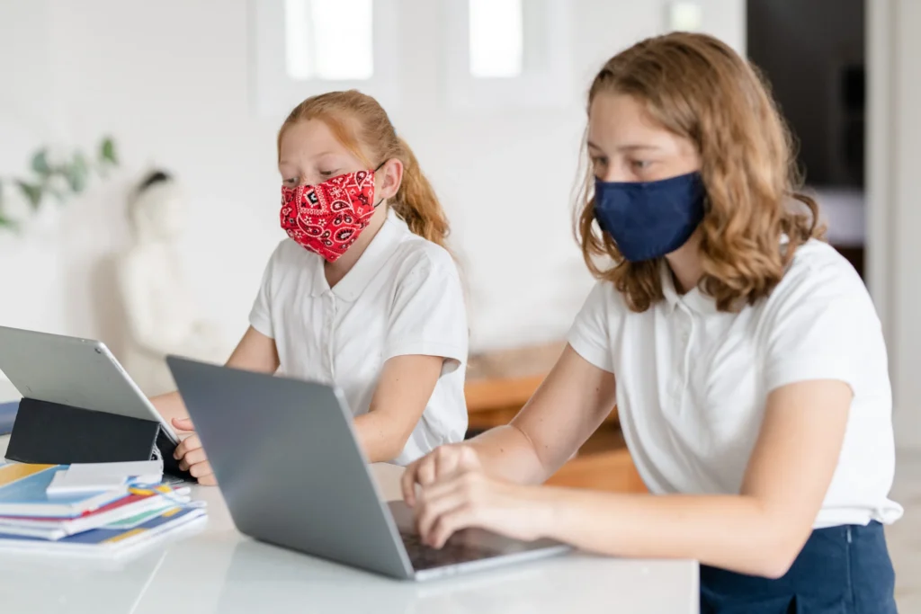 Two female students wearing face mask in the classroom with laptops