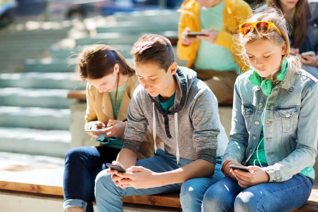 Teenagers sitting at a bench looking at their smart phones.