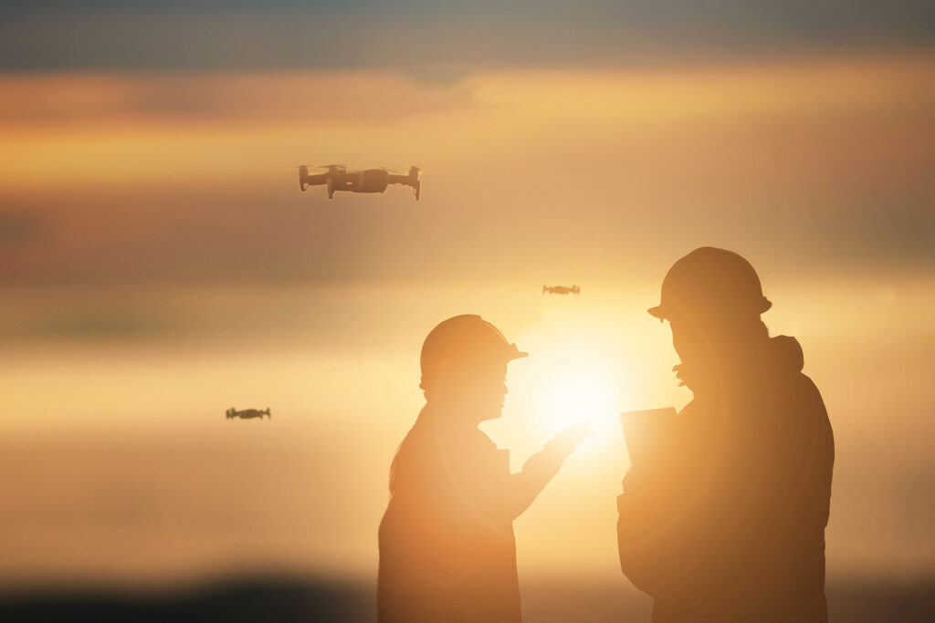 Two people wearing hard hats with drones and a sunset in the background.