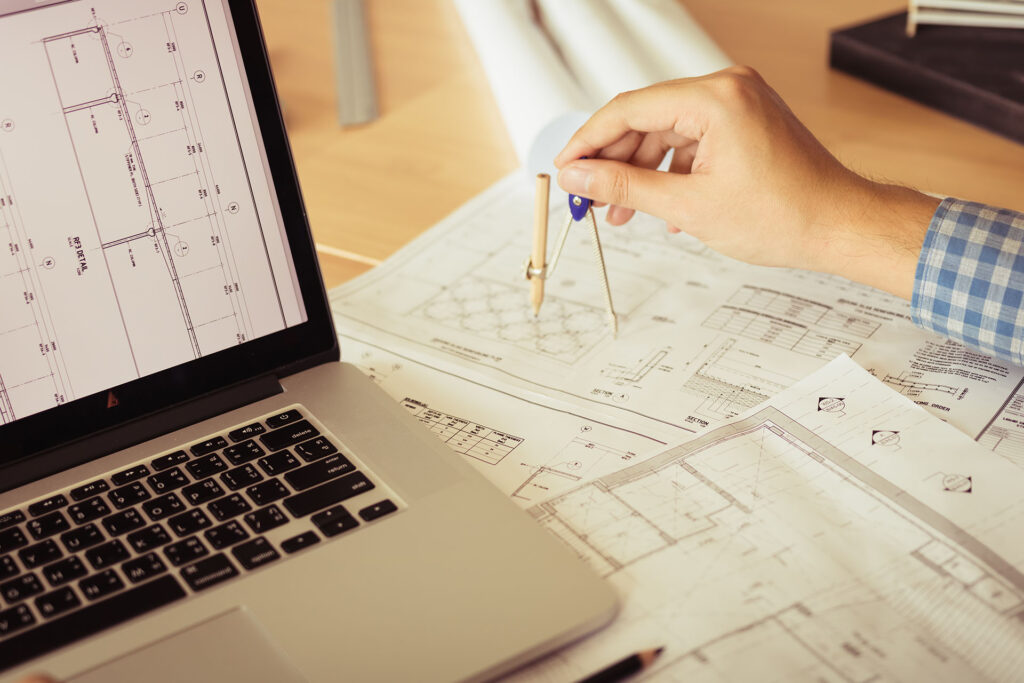 Architect working on blueprint in workplace with a laptop