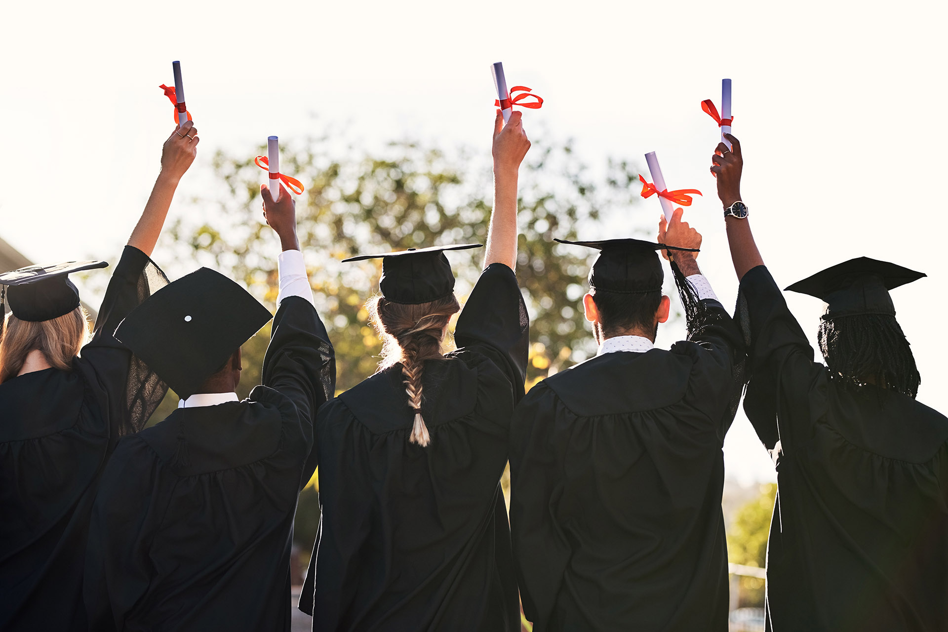 Group of students in graduation caps and gowns holding diplomas outdoors.