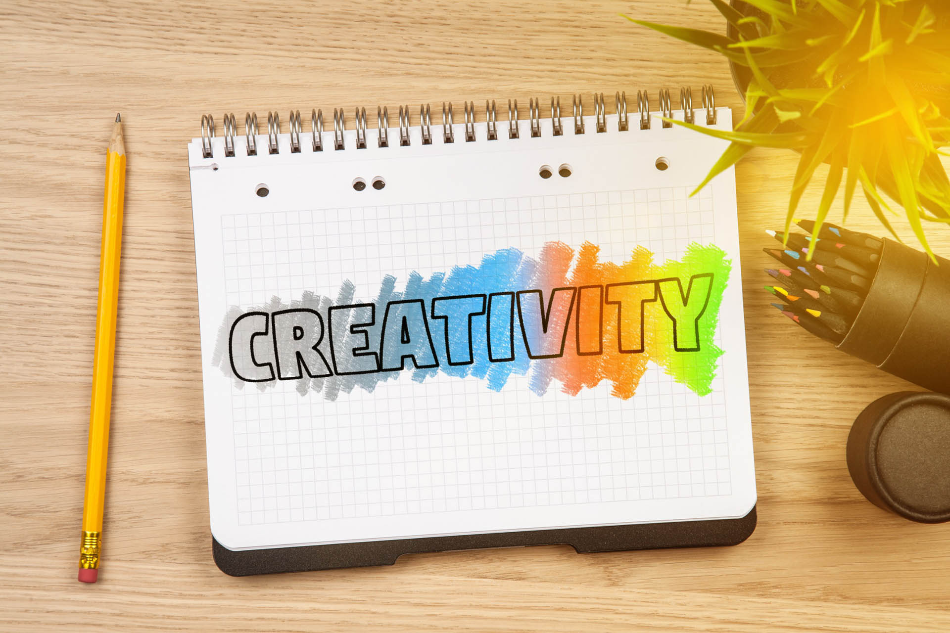 Notepad with the word “creativity” next to a pencil, plant, and cup of colored pencils.