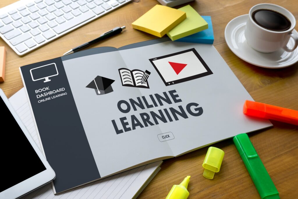 Words “online learning” on a piece of paper with images of a graduation cap, a book, and a video next to highlighters, a keyboard, an iPad, and a cup of coffee.
