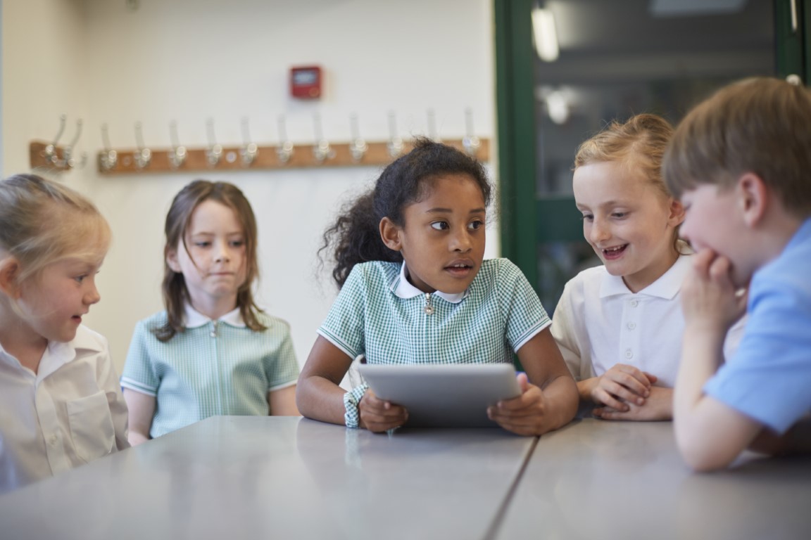 Schoolchildren gather around a digital tablet in a classroom.