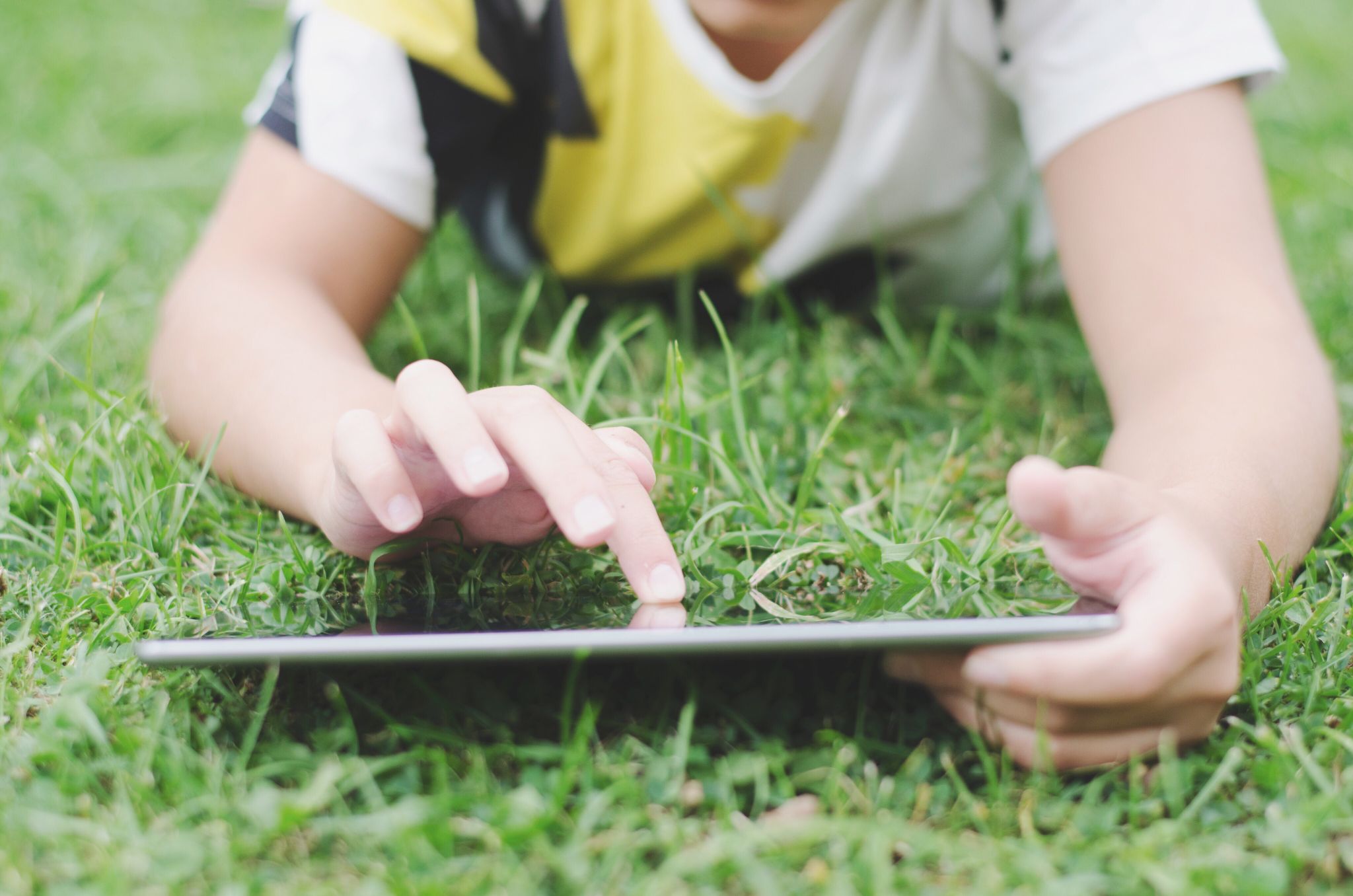 Child lying in the grass while using an iPad.
